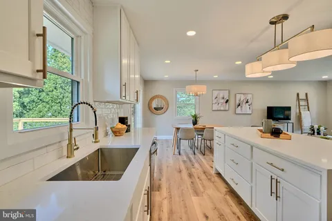 a large kitchen with stainless steel appliances a large counter space a sink dishwasher and white cabinets with wooden floor