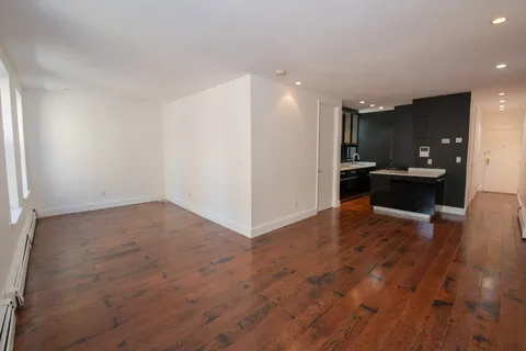 an empty room with wooden floor and kitchen view