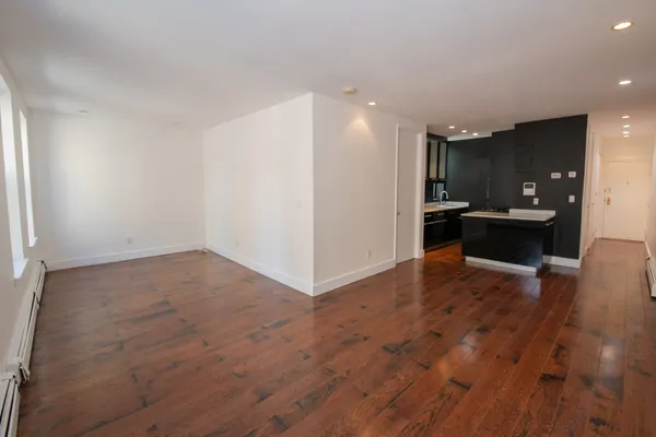 an empty room with wooden floor and kitchen view
