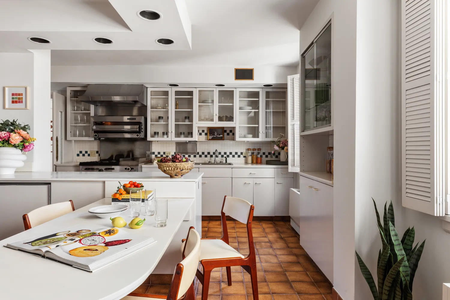 a white kitchen with a stove a sink and a dining table with wooden floor