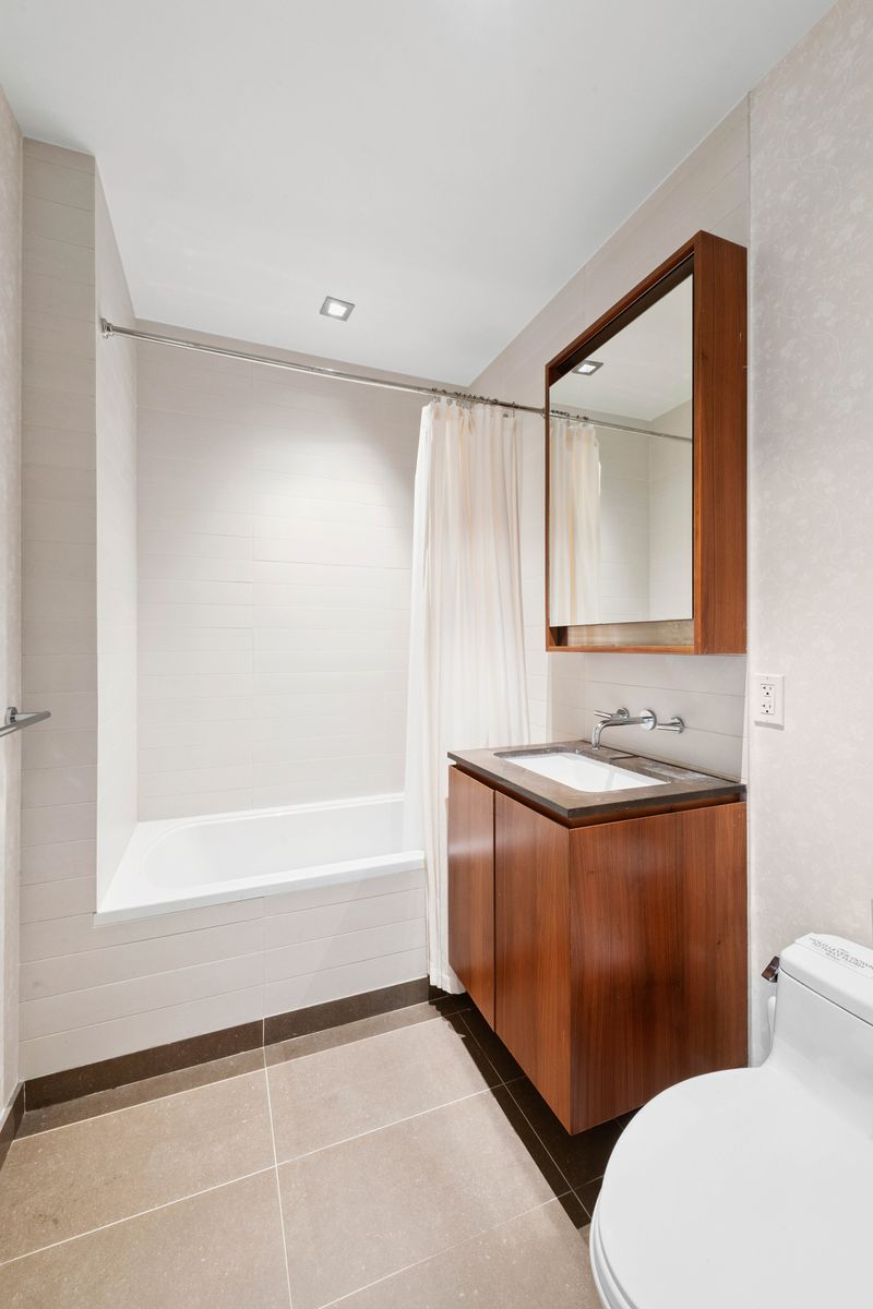555 West 59th Street, Unit 25E Manhattan, NY 10019 - Photo 9 of 18 a bathroom with a granite countertop sink a mirror and a bathtub