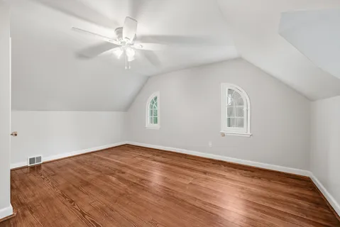 an empty room with wooden floor chandelier fan and windows
