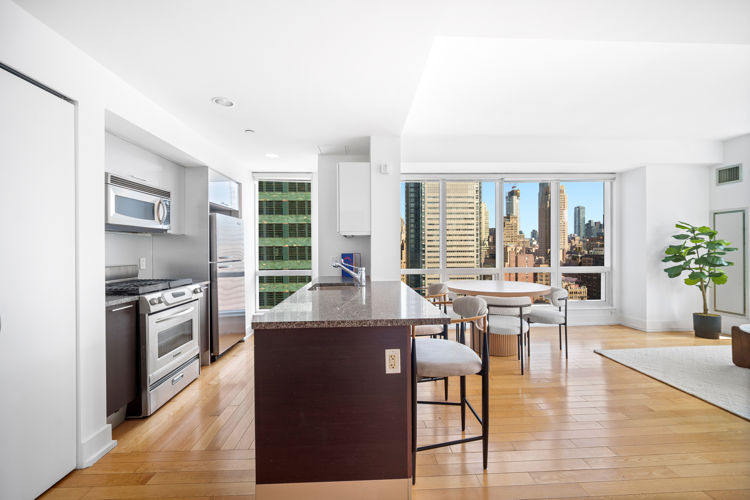 350 West 42nd Street, Unit 27K Manhattan, NY 10036 - Photo 6 of 18 a kitchen with granite countertop a stove top oven a sink dishwasher and a dining table with wooden floor