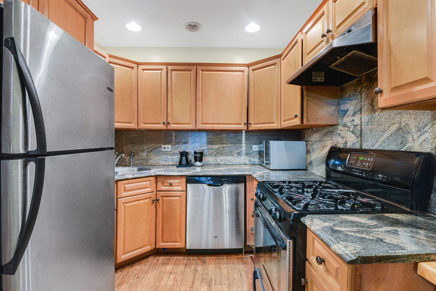 a kitchen with stainless steel appliances granite countertop a stove a sink dishwasher and refrigerator with wooden floor