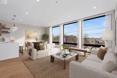 a living room with furniture large windows and a view of kitchen