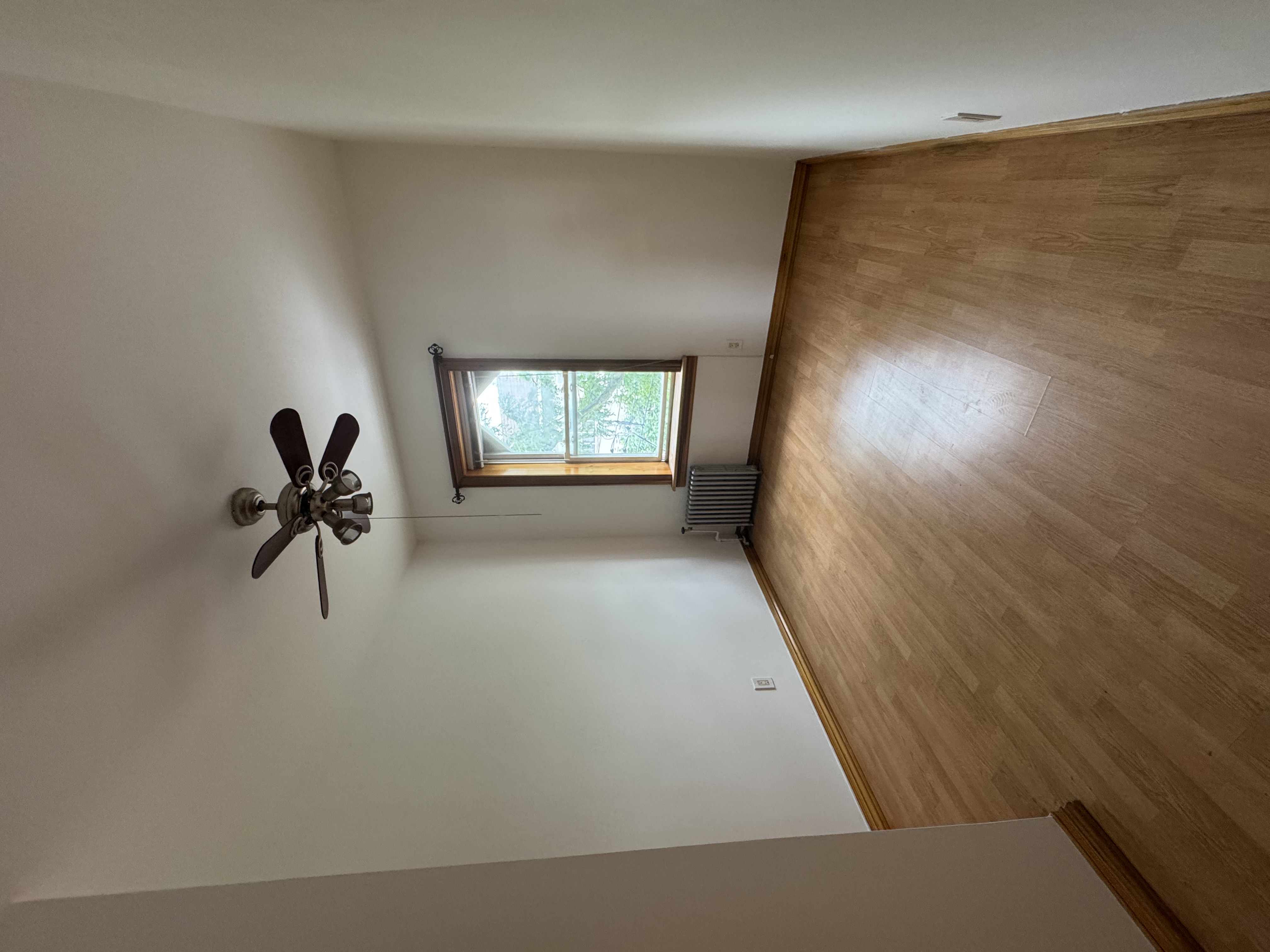 60-27 56th Road, Unit 3 Queens, NY 11378 - Photo 4 of 9 an empty room with wooden floor chandelier fan and windows