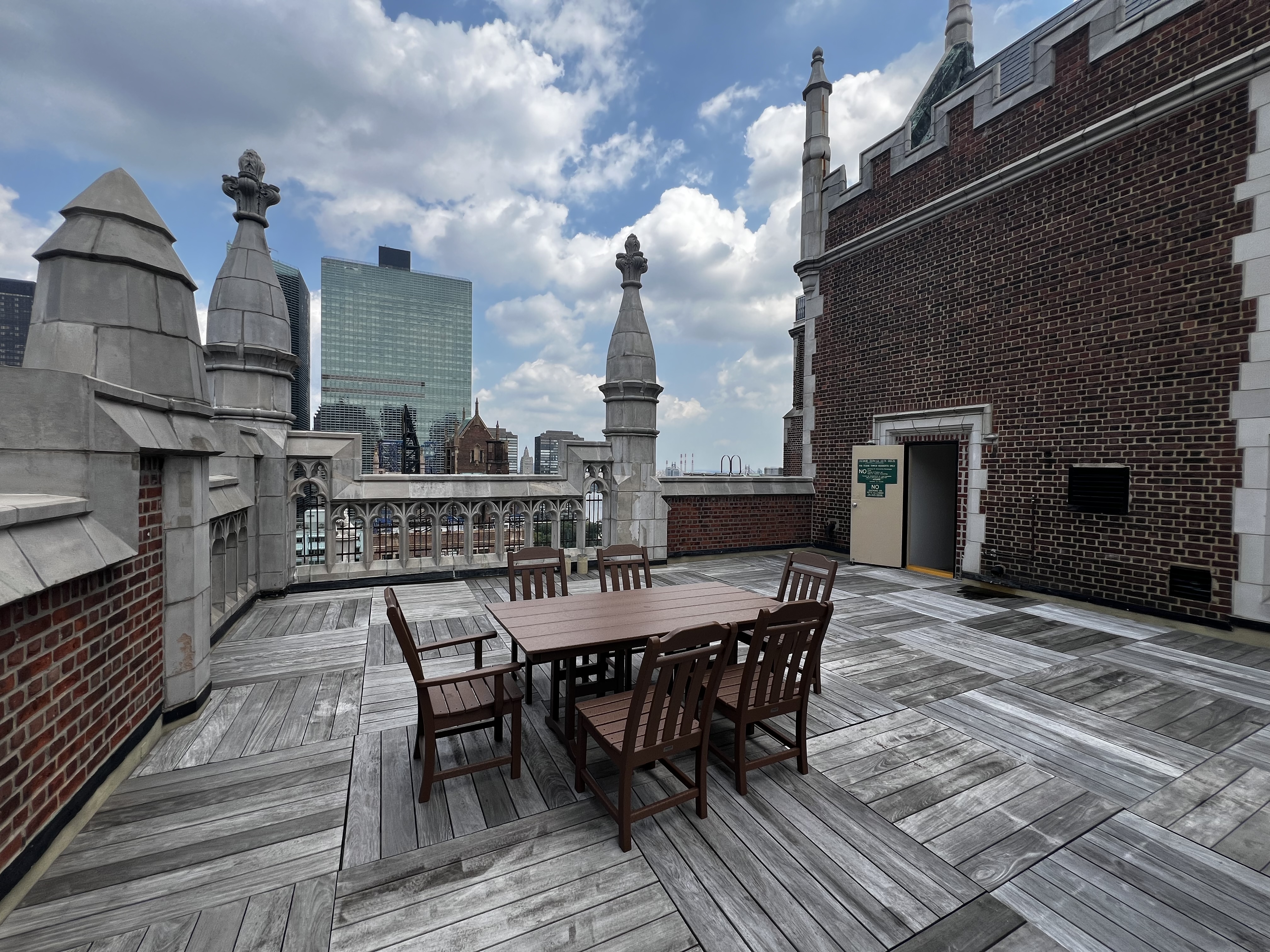 25 Tudor City Place, Unit 508 Manhattan, NY 10017 - Photo 14 of 17 a view of a roof deck with table and chairs a barbeque with wooden floor and fence
