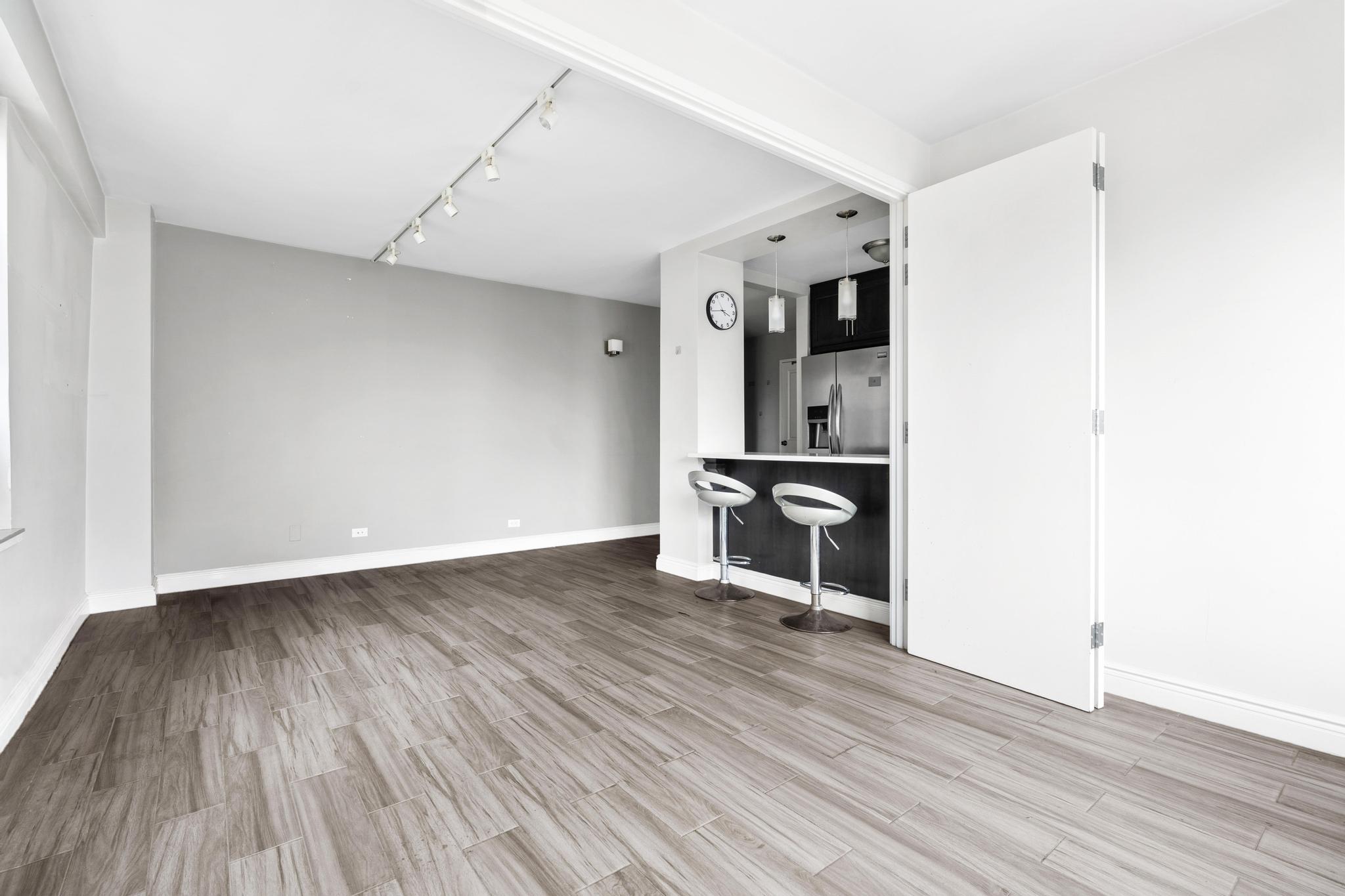 266 East Broadway, Unit 1304B Manhattan, NY 10002 - Photo 4 of 8 an empty room with wooden floor and a ceiling fan