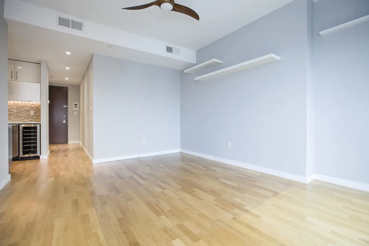 an empty room with wooden floor kitchen view and windows