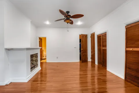 a view of an empty room with wooden floor and a ceiling fan