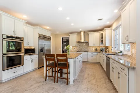 a large kitchen with stainless steel appliances granite countertop a stove top oven a sink dishwasher and white cabinets
