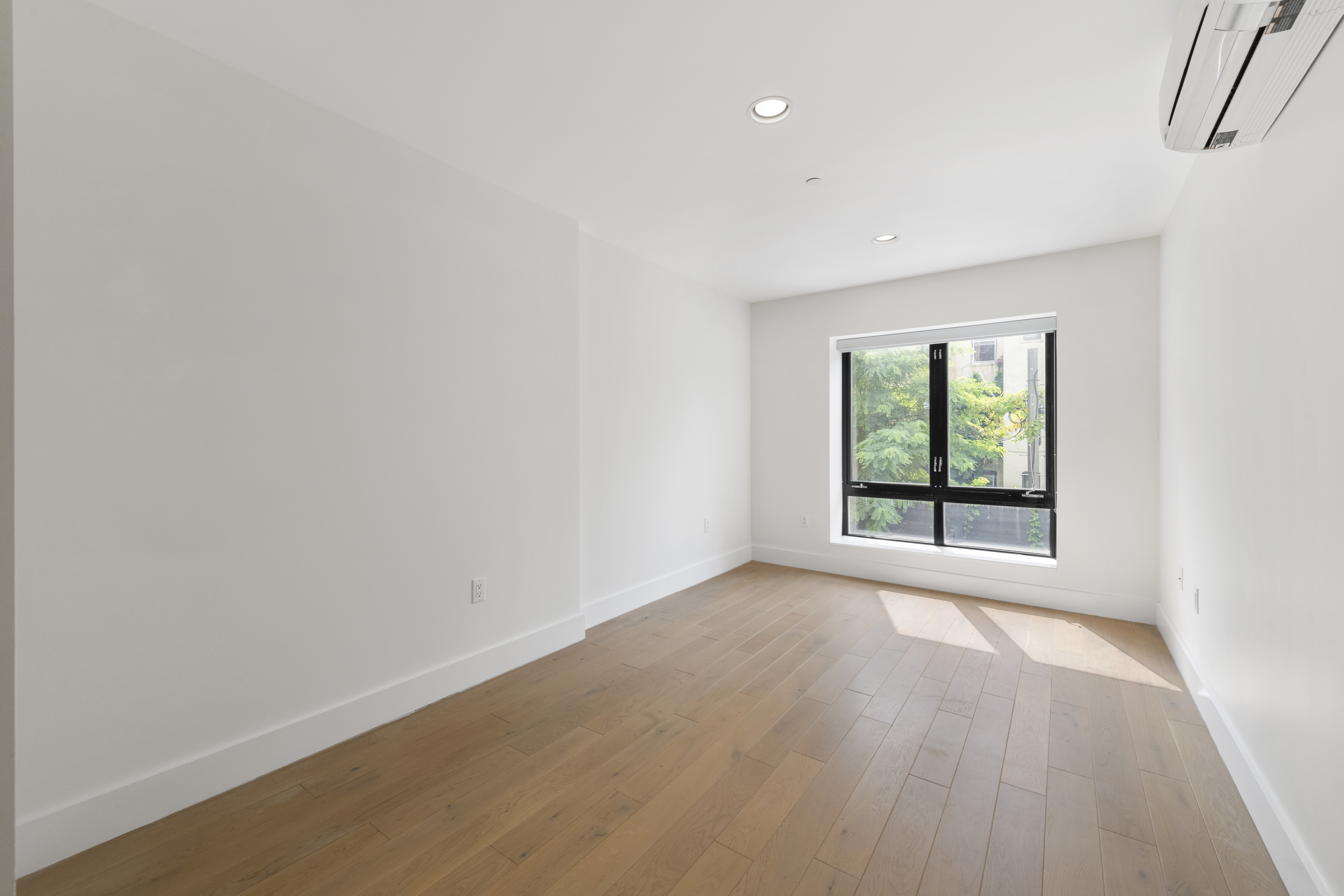 a view of an empty room with wooden floor and a window