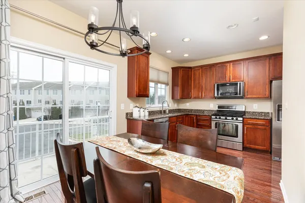 a kitchen with stainless steel appliances granite countertop a stove top oven a sink dishwasher a dining table and chairs with wooden floor