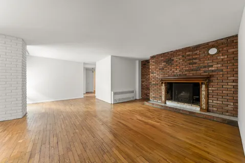 a view of an empty room with wooden floor fireplace and a window