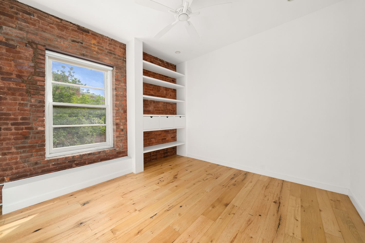 a view of empty room with wooden floor and fan