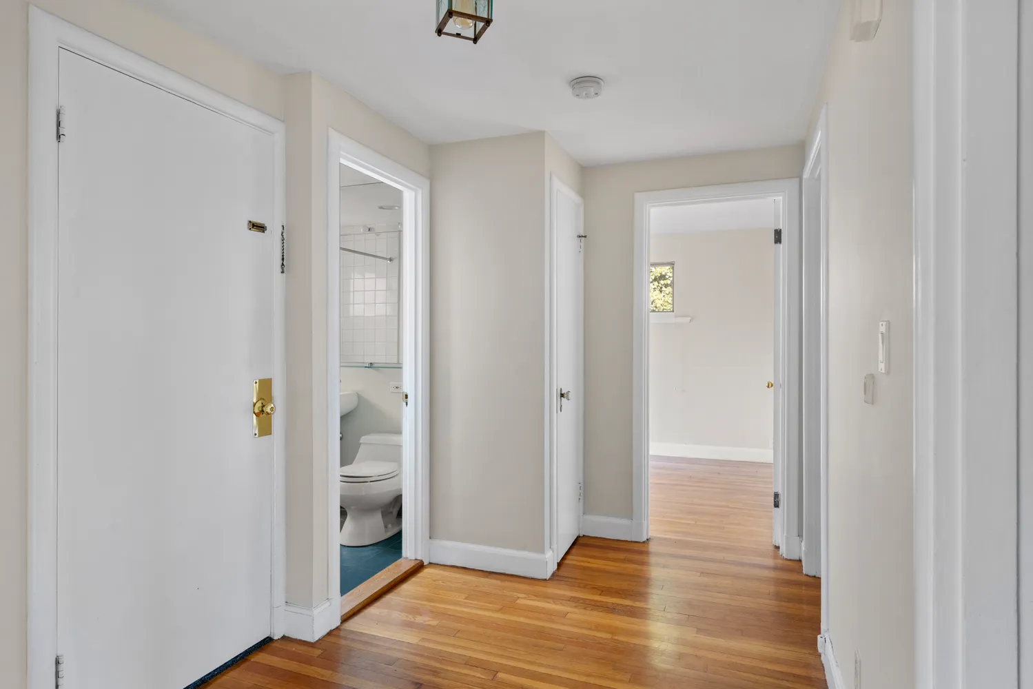 a view of an empty room with wooden floor and a bathroom