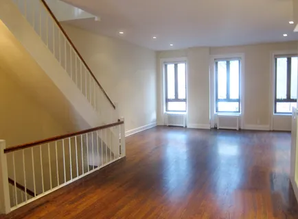 a view of an empty room with wooden floor and fan
