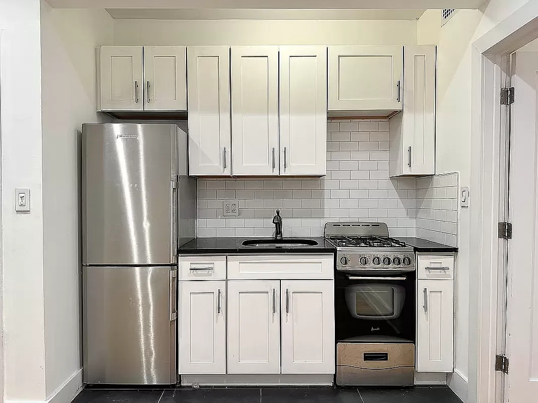 1582 York Avenue, Unit 2C Manhattan, NY 10028 - Photo 5 of 12 a kitchen with granite countertop a refrigerator stove and white cabinets