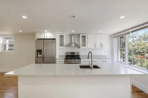 a kitchen with granite countertop a stove a sink a refrigerator and white cabinets with wooden floor