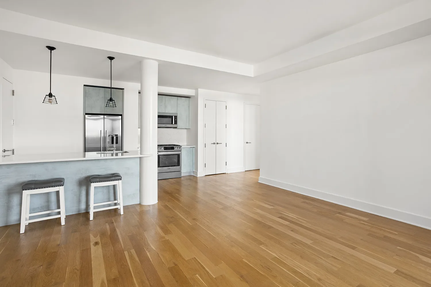 a view of empty room with wooden floor and kitchen view