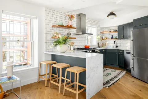 a kitchen with stainless steel appliances granite countertop a stove a sink a microwave refrigerator and a dining table with wooden cabinet