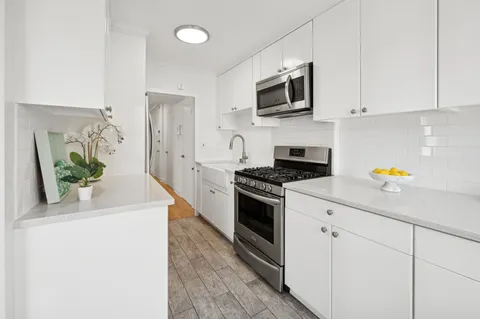 a kitchen with stainless steel appliances a stove a microwave a sink and white cabinets