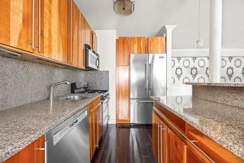 a kitchen with stainless steel appliances granite countertop a sink a refrigerator and wooden cabinets