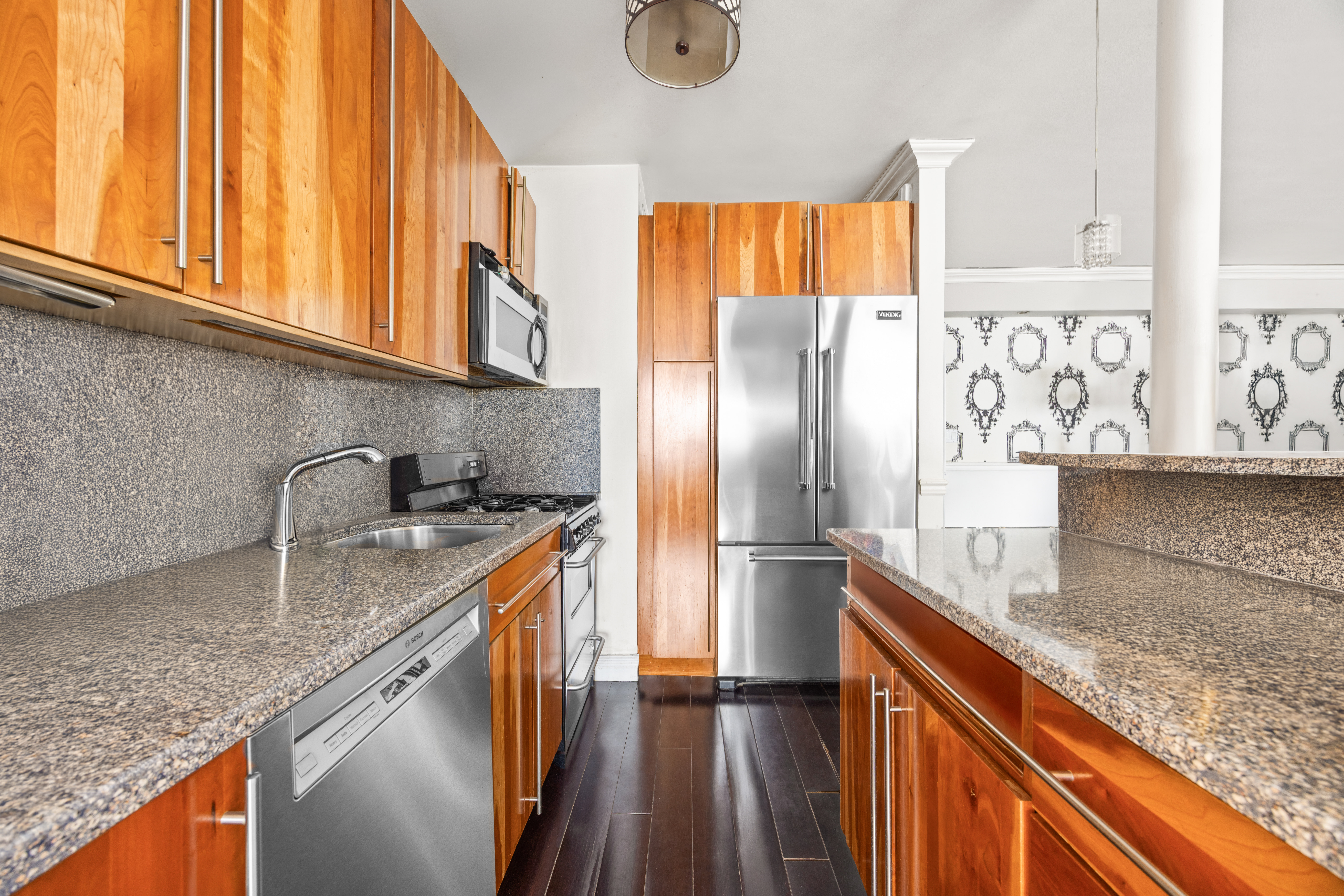 136 East 56th Street, Unit 10JK Manhattan, NY 10022 - Photo 3 of 12 a kitchen with stainless steel appliances granite countertop a sink a refrigerator and wooden cabinets