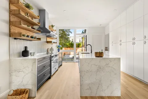 a large white kitchen with stainless steel appliances granite countertop a large counter top a stove and a wooden floors