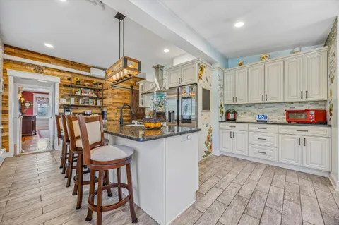 a open kitchen with stainless steel appliances granite countertop a refrigerator a stove and white cabinets with wooden floors