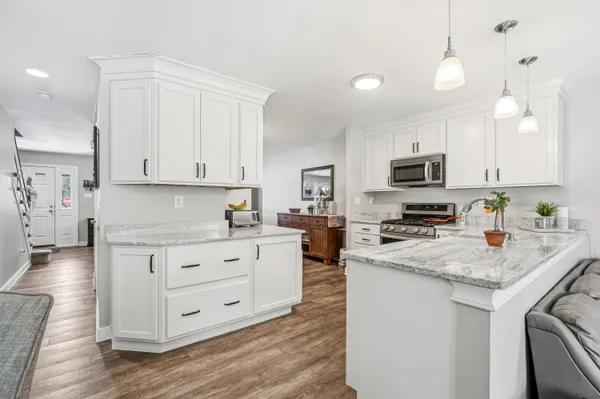 a kitchen with granite countertop white cabinets white appliances a sink and a wooden floor