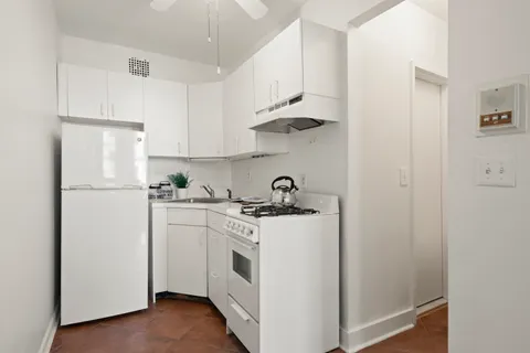 a kitchen with a white stove refrigerator and white cabinets with wooden floor