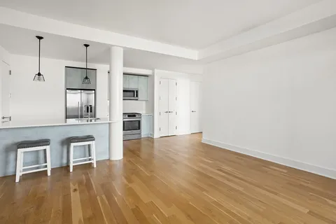 a view of empty room with wooden floor and kitchen view