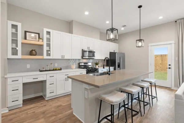 a kitchen with stainless steel appliances granite countertop a stove top oven a refrigerator a sink and white cabinets with wooden floor