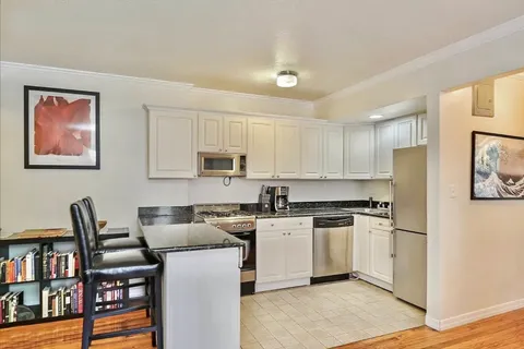 a kitchen with stainless steel appliances granite countertop a stove top oven a sink a refrigerator white cabinets and wooden floor