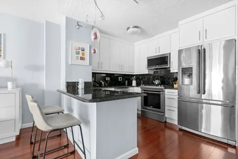 a kitchen with a refrigerator a microwave a stove and white cabinets with wooden floor