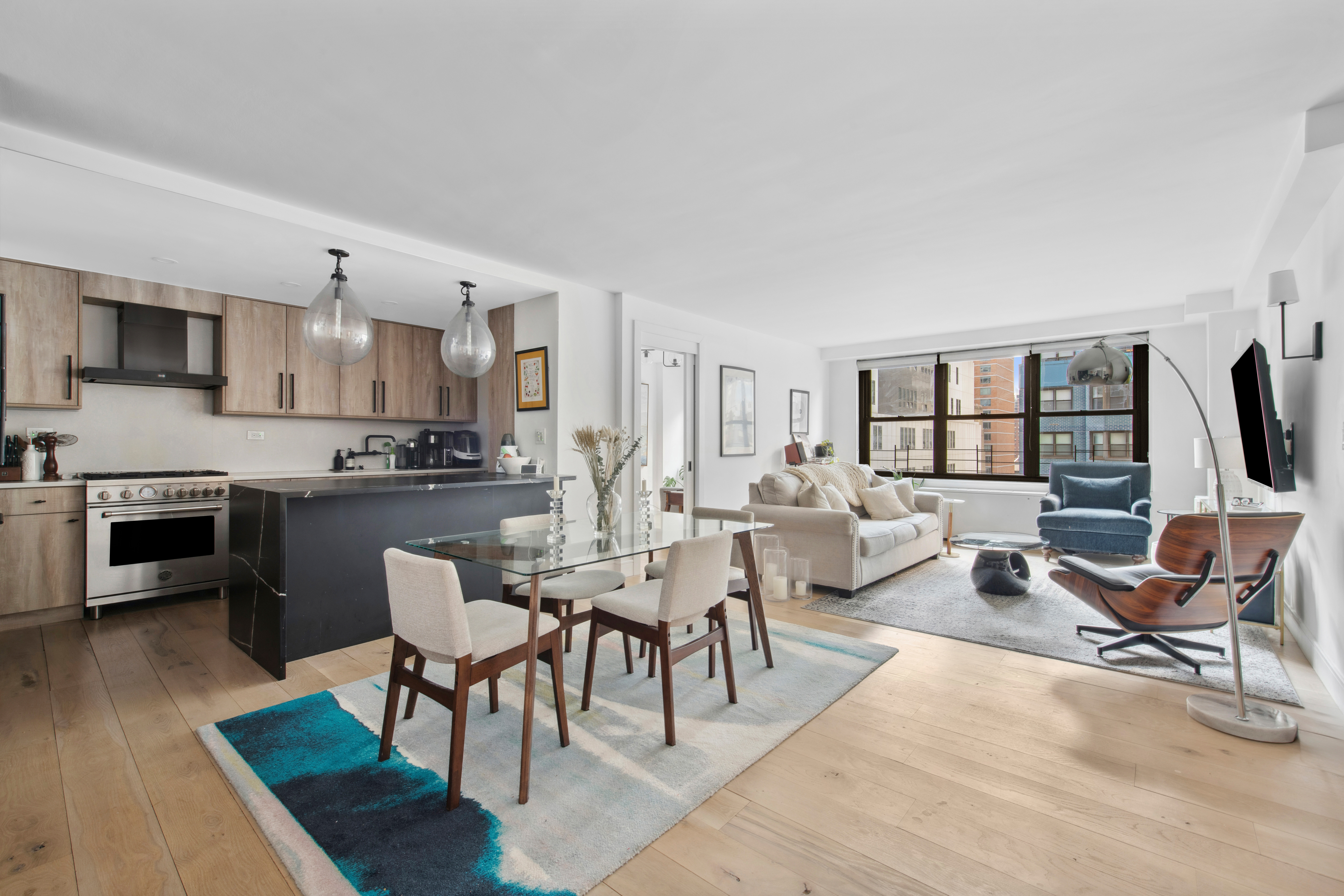 a living room with furniture a rug kitchen view and a large window