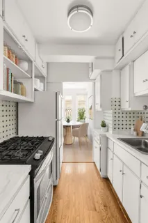 a kitchen with stainless steel appliances a white stove top oven a sink a refrigerator and white cabinets with wooden floor