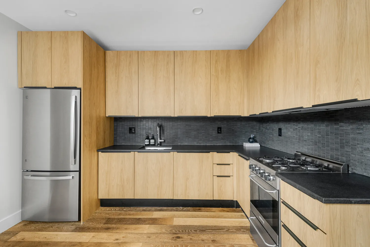 a kitchen with stainless steel appliances granite countertop a refrigerator a stove and a sink with wooden cabinets