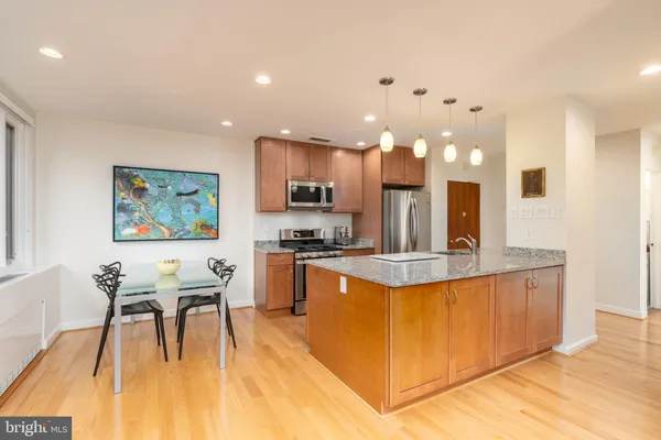 a dining hall with stainless steel appliances granite countertop a kitchen island a stove a refrigerator a sink a dining table and chairs with wooden floor