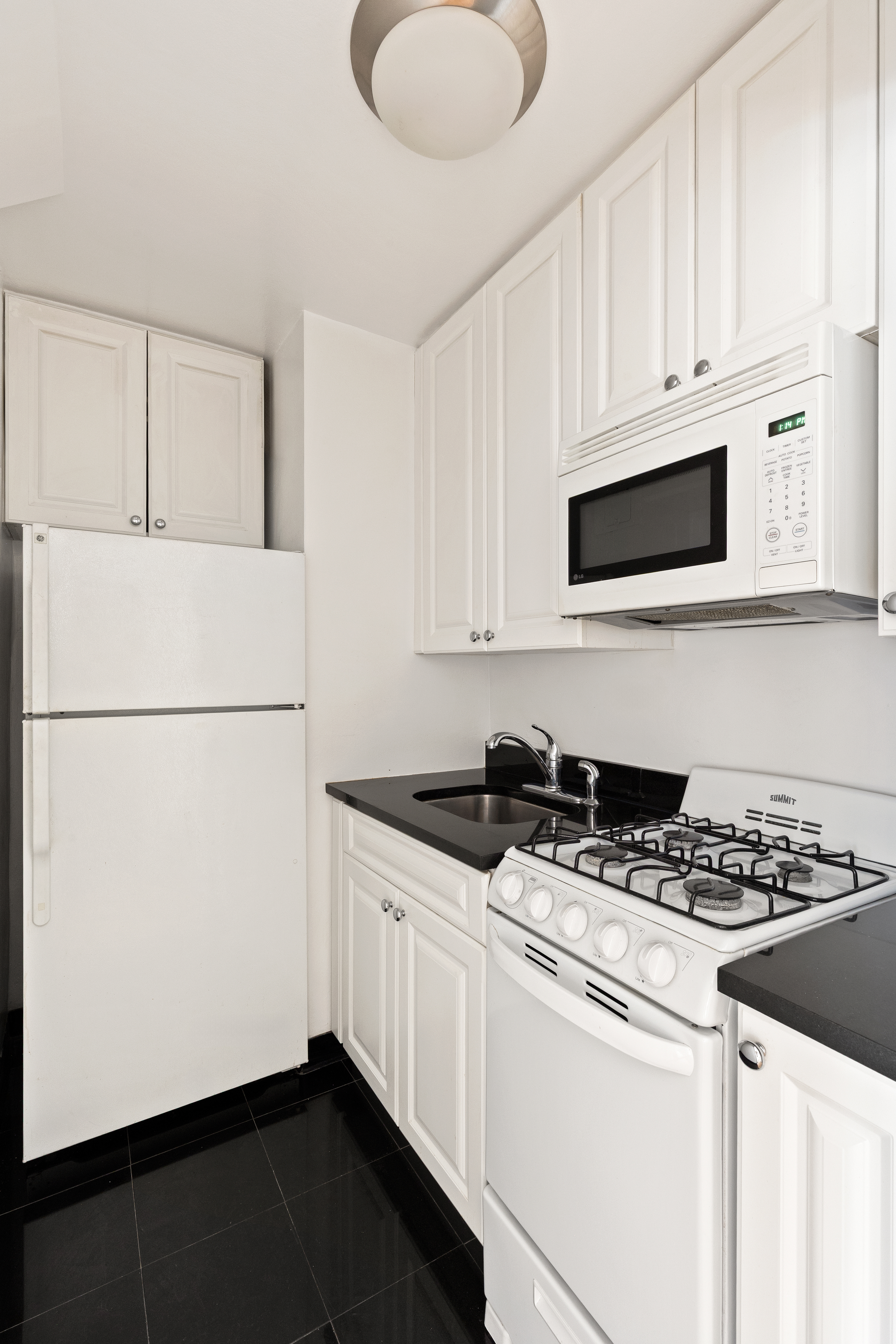310 East 70th Street, Unit 2F Manhattan, NY 10021 - Photo 3 of 8 a kitchen with granite countertop white cabinets and black appliances
