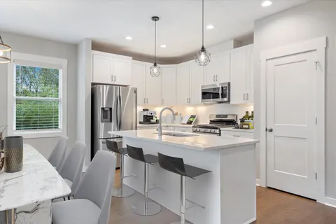 a kitchen with stainless steel appliances granite countertop a refrigerator a stove a sink a dining table and chairs with wooden floor