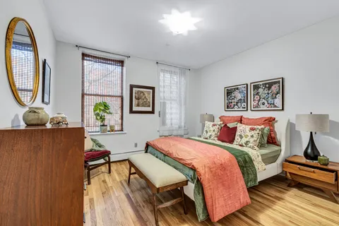 a bedroom with a bed a painting on the wall and a potted plant