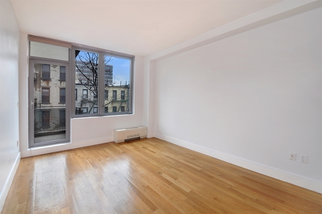 117 West 123rd Street, Unit 4B Manhattan, NY 10027 - Photo 4 of 16 a view of an empty room with window and wooden floor