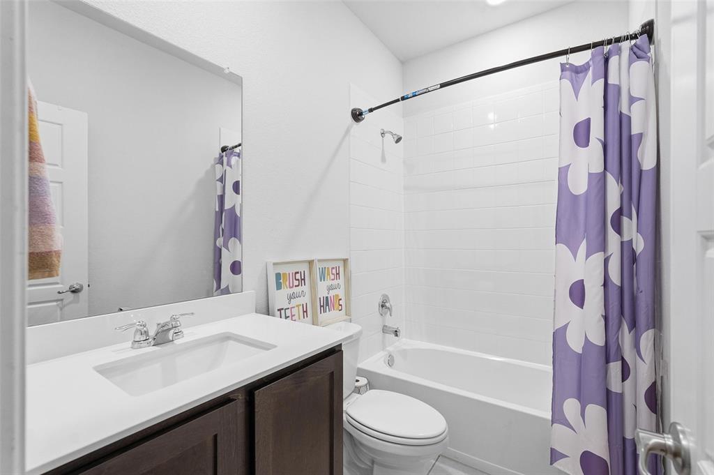 949 Philadelphia Street Fate, TX 75189 - Photo 24 of 36 a bathroom with a granite countertop sink a toilet a shower curtain and a bath tub