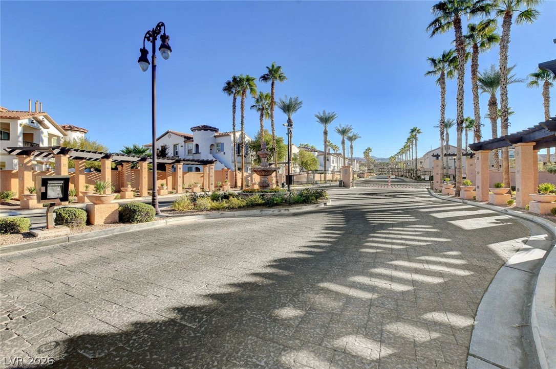 48 Jasmine Point Street Henderson, NV 89074 - Photo 11 of 62 An inviting community entrance features a decorative fountain and lush palm trees lining the paver-patterned roadway.