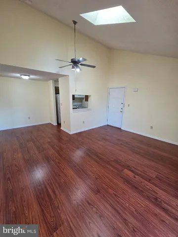 an empty room with wooden floor ceiling fan and kitchen view