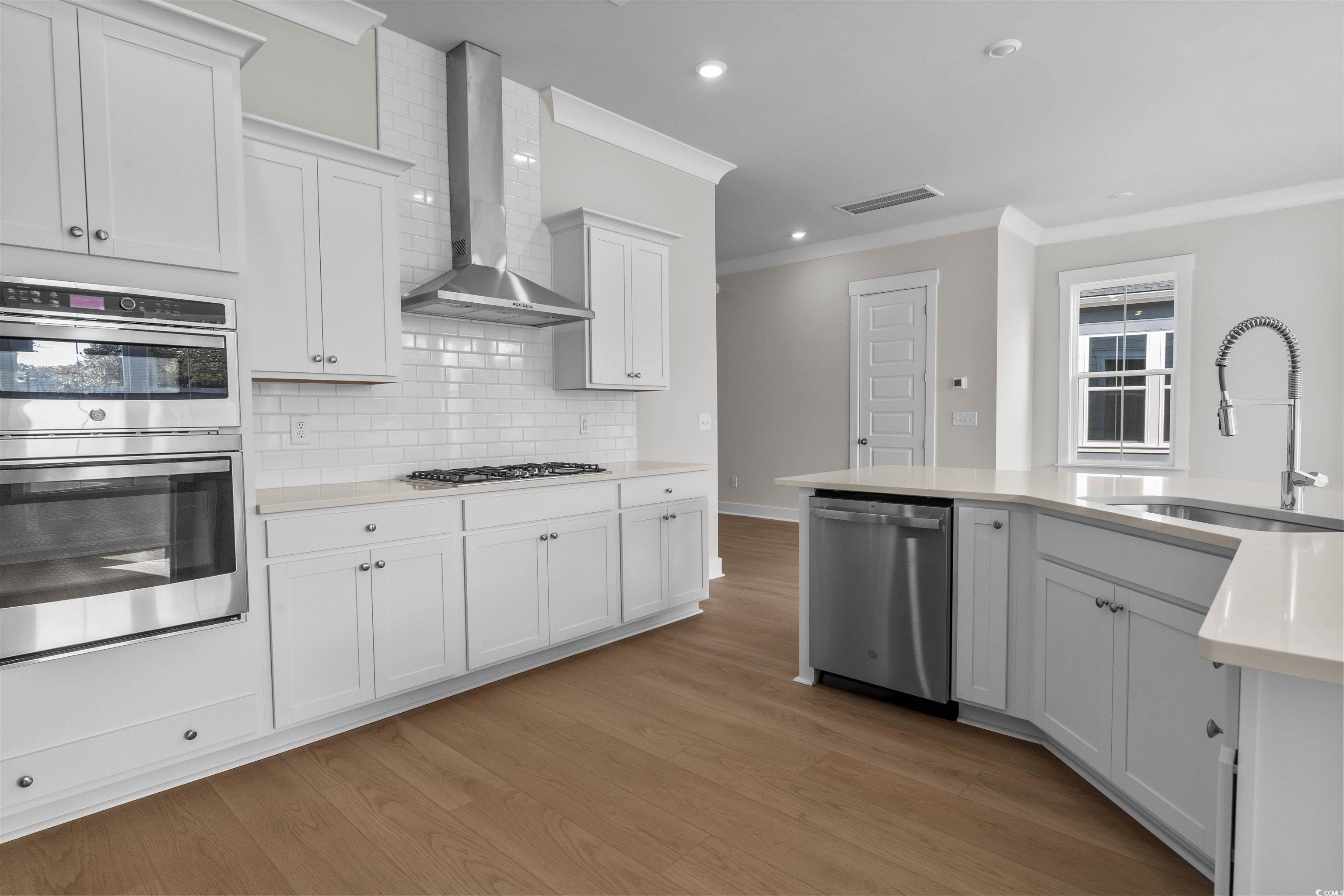 229 Atlantic Breeze Street Myrtle Beach, SC 29572 - Photo 15 of 24 Kitchen with appliances with stainless steel finishes, white cabinetry, ornamental molding, wall chimney range hood, and recessed lighting