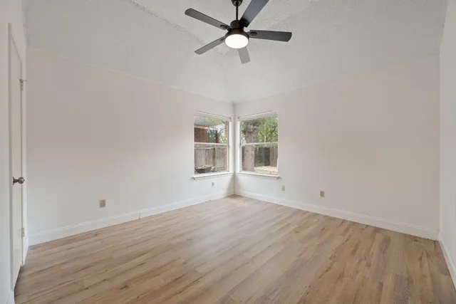 an empty room with wooden floor fan and windows