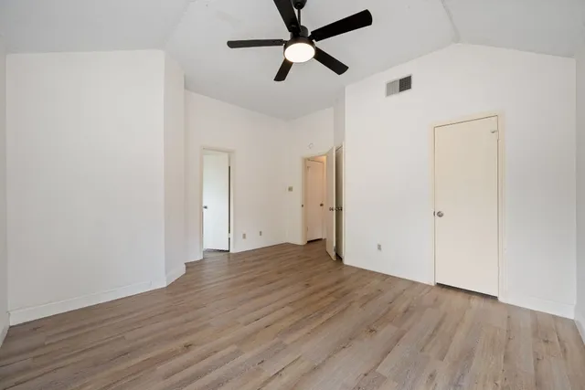 an empty room with wooden floor ceiling fan and windows